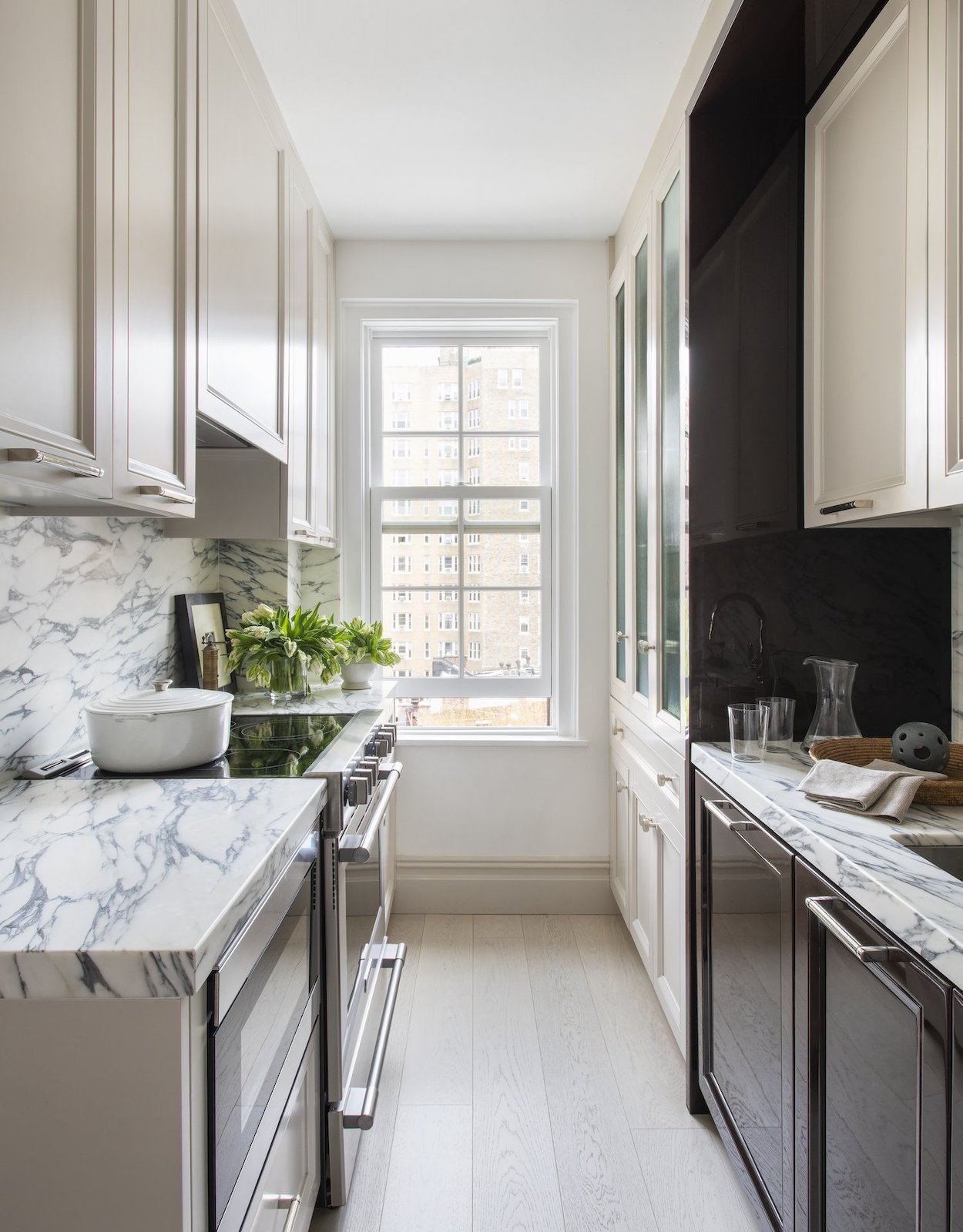 A galley kitchen a white and dark grey marble countertop and matching backsplash.