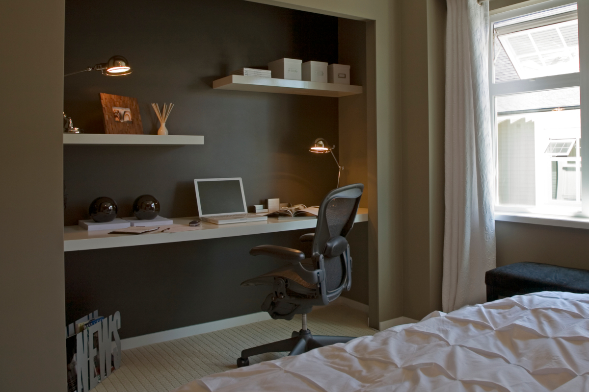 A long desk and two floating shelves are built into the back wall of a modern bedroom's converted reach-in closet.