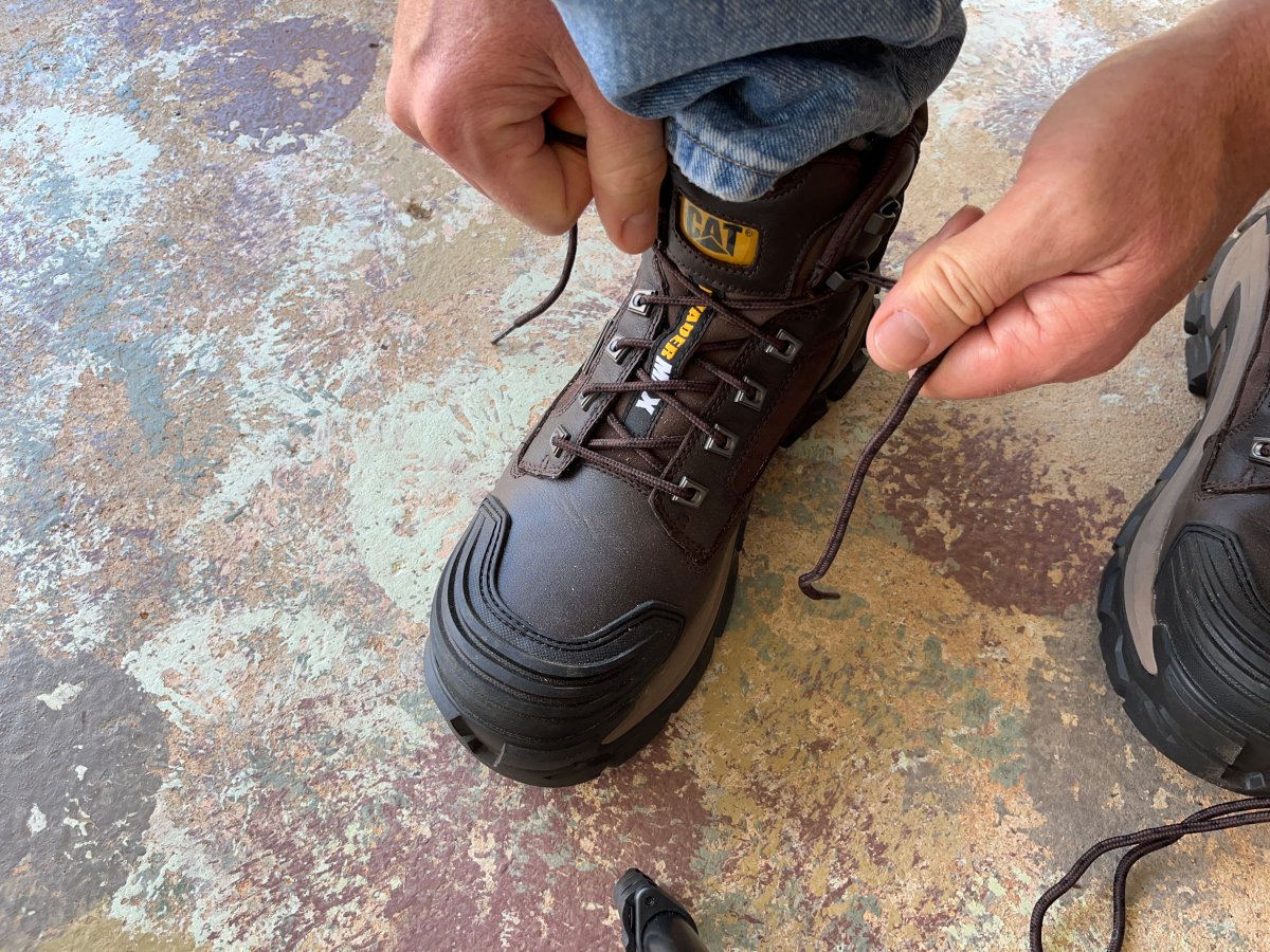 Man lacing up CAT Invader Max boots in a garage