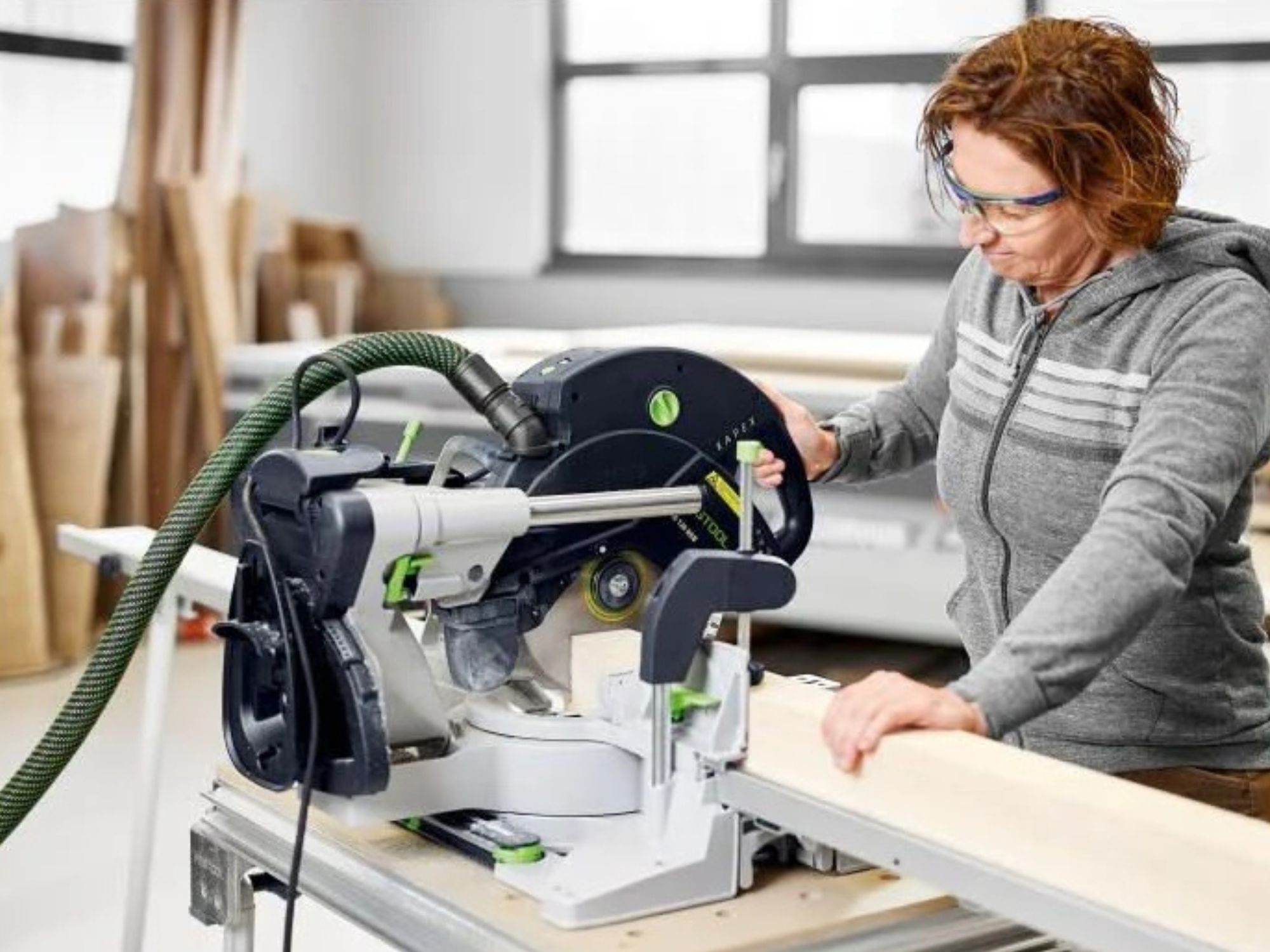 Person in gray hoodie cutting dimensional lumber with a Festool sliding compound miter saw