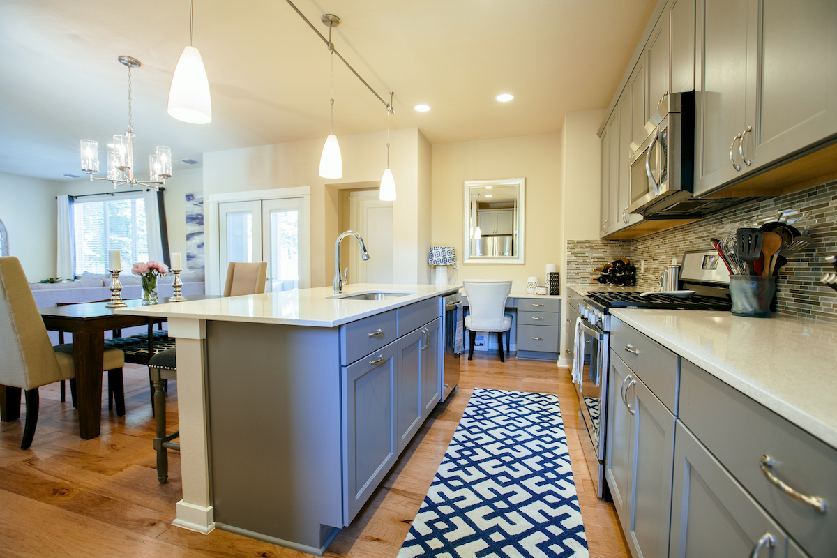 A galley kitchen with hardwood floor and grey cabinets has a blue runner between the island and counter.