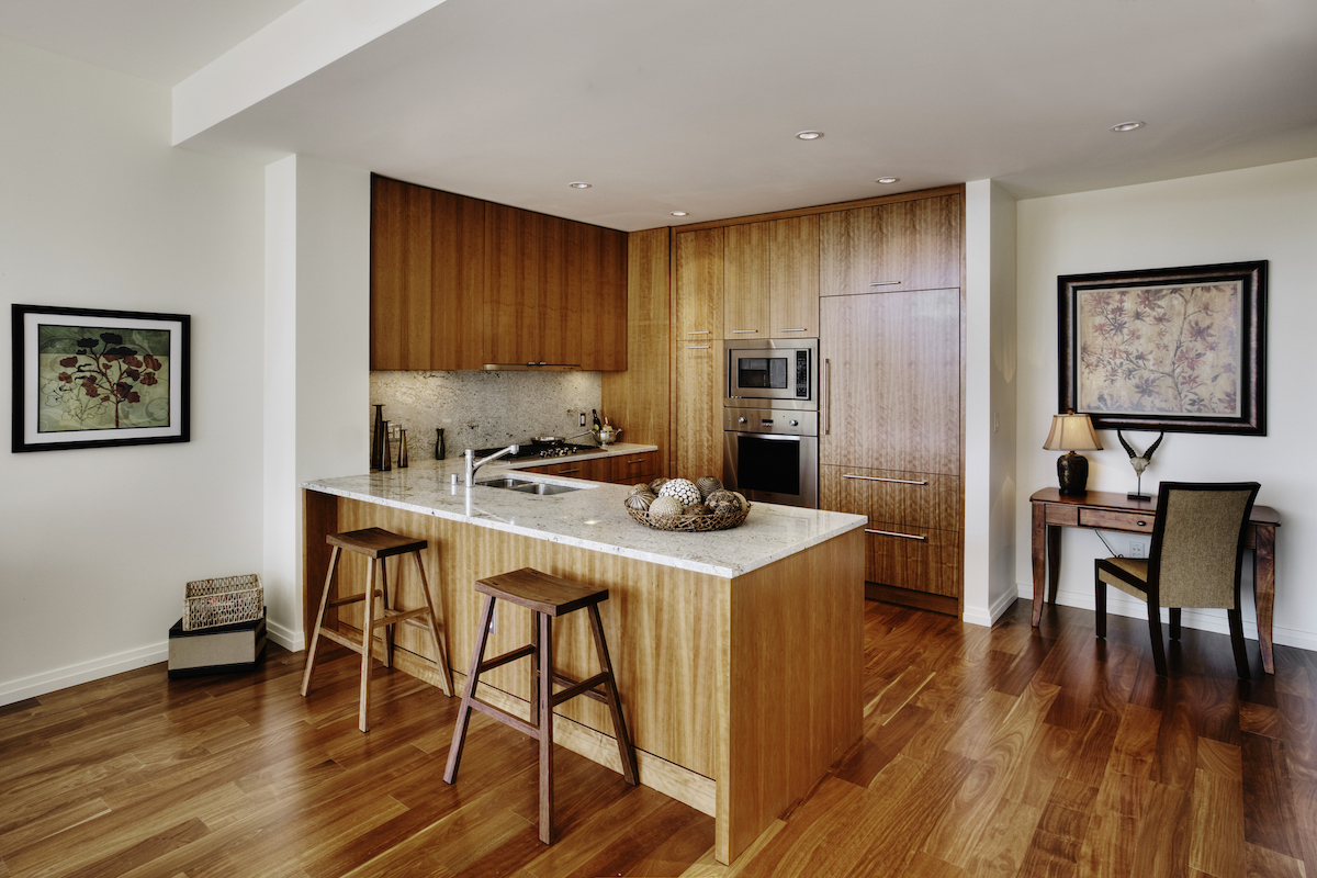 A modern galley kitchen with hardwood floor has a matching wood pattern on the kitchen cabinets.