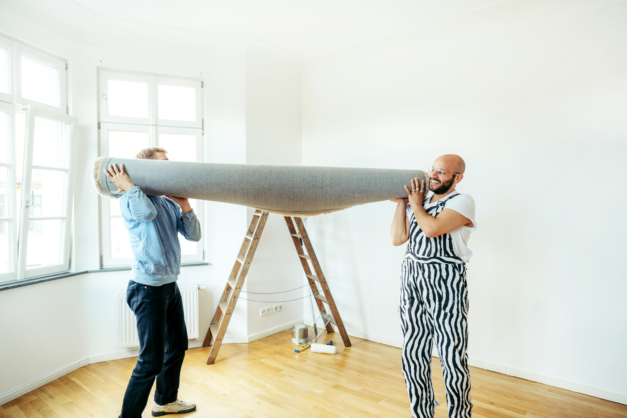 Two men carrying a carpet out of a room.