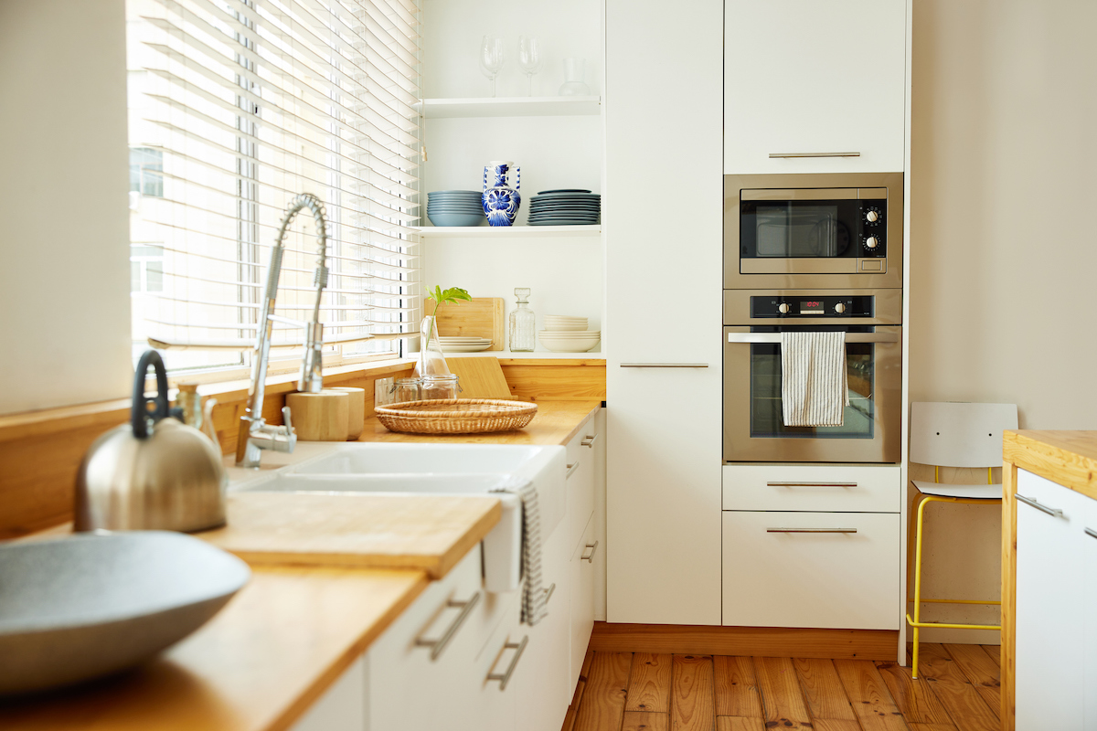 A galley kitchen is consistently cream and natural wood-colored in cabinets, countertops, and flooring.