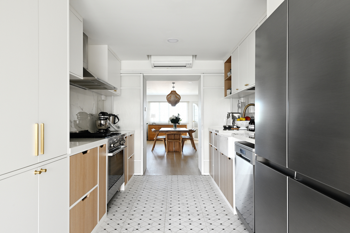 A galley kitchen with stainless steel appliances features a white tile floor with a black geometric pattern.