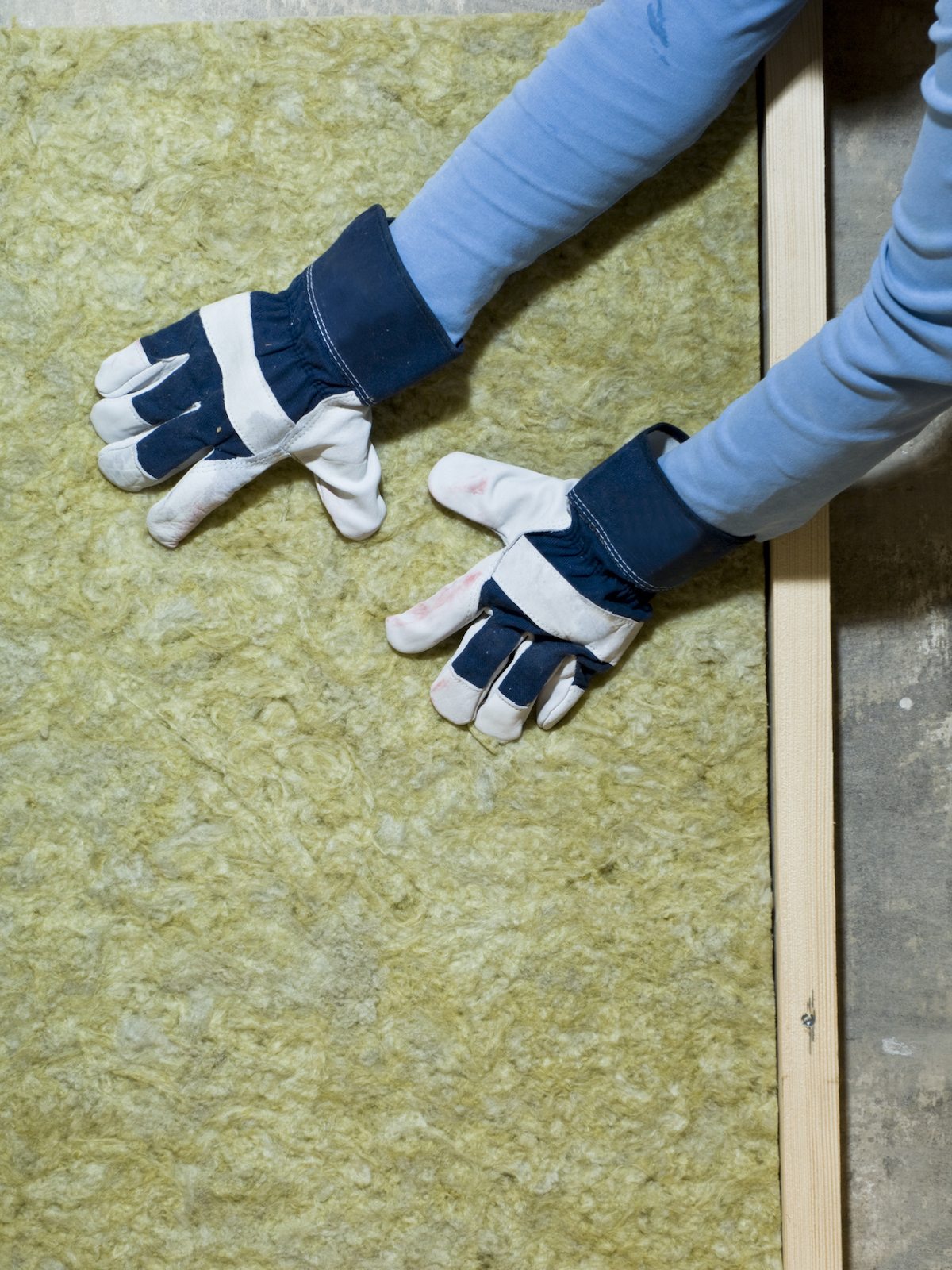 A person wearing gloves is pressing on yellow insulation into a wall frame. 