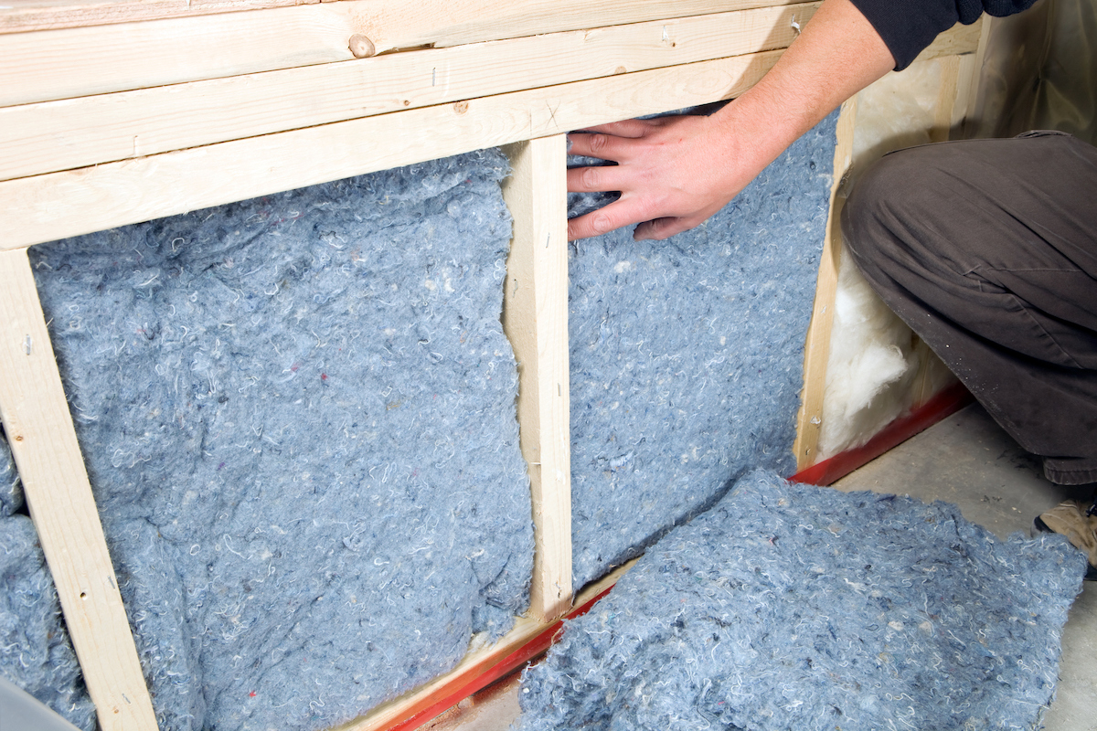 A person is installing blue jean denim insulation into a wall.