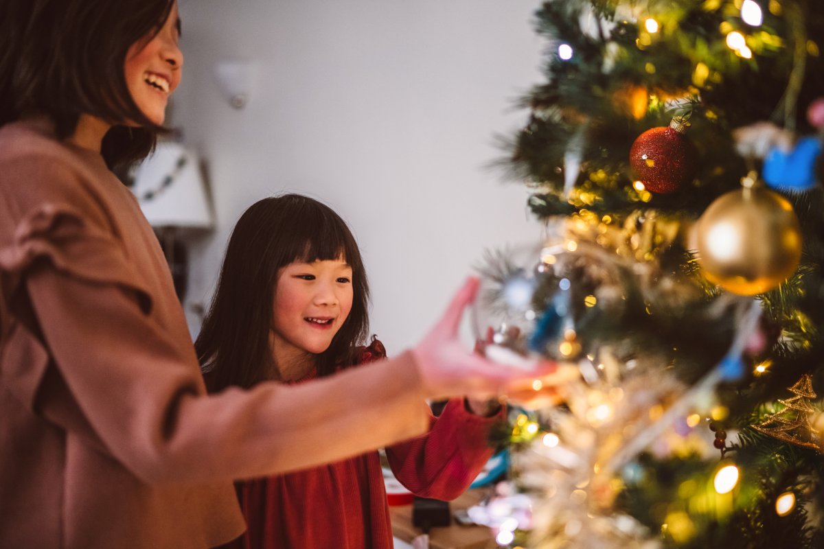 Two cheerful young sisters hanging Christmas ornaments on the Christmas tree at home.