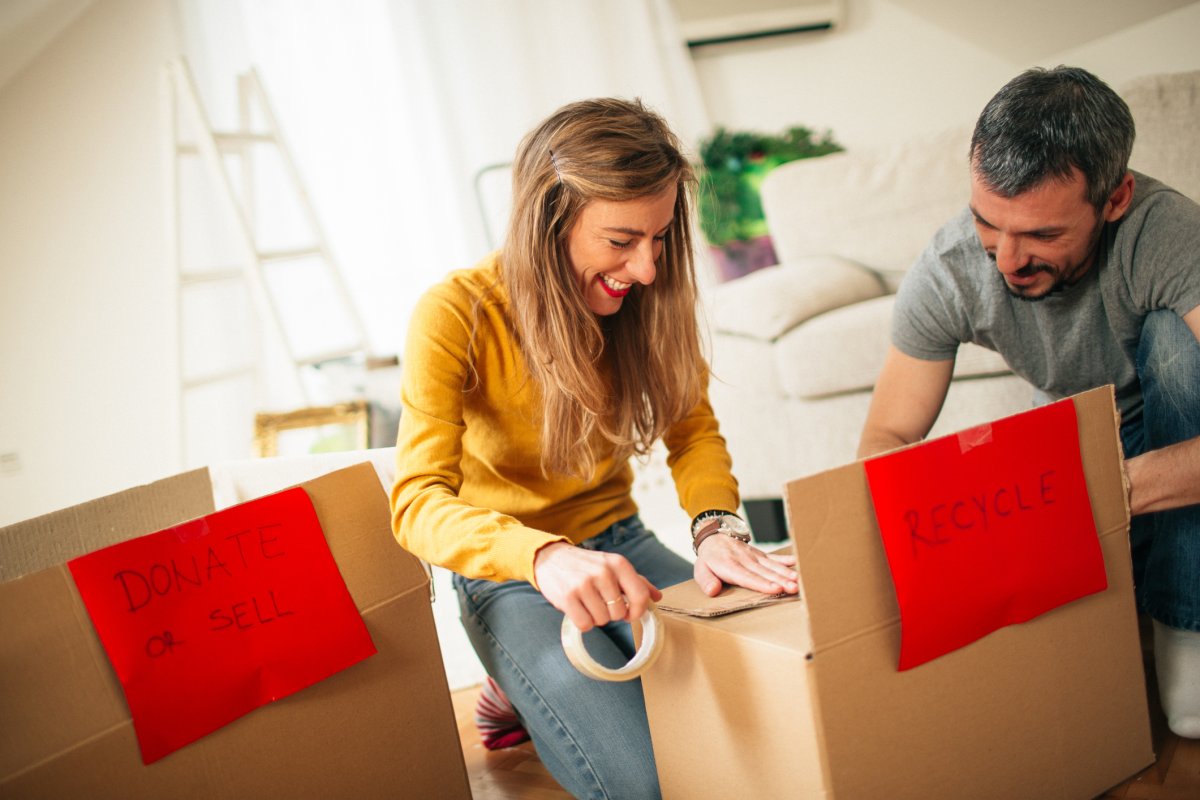 Happy couple packing boxes that say donate, sell, or recycle.