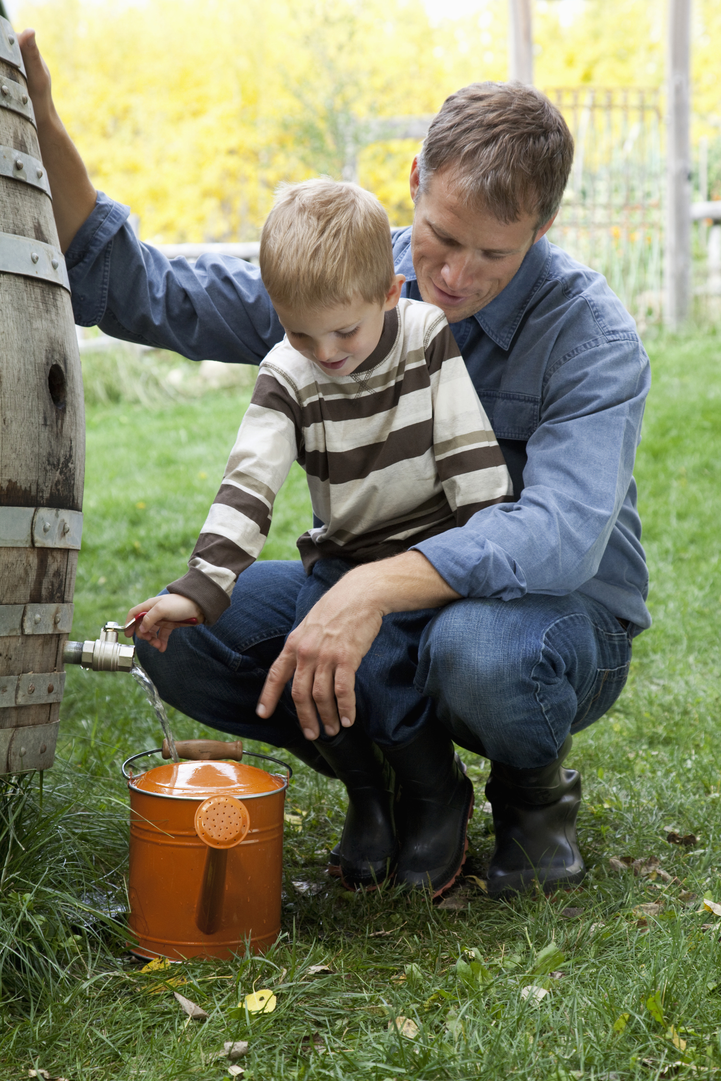 A father and son filling a watering can from their home rain barrel.