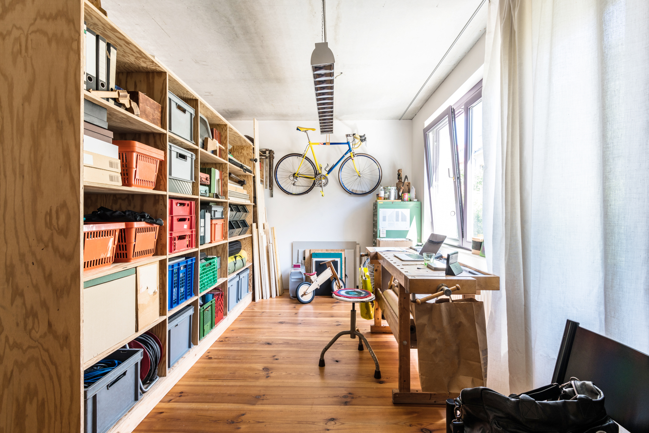 A narrow home office in a converted garage uses the colorful contents of custom shelving behind a well-lit desk as a meeting backdrop.