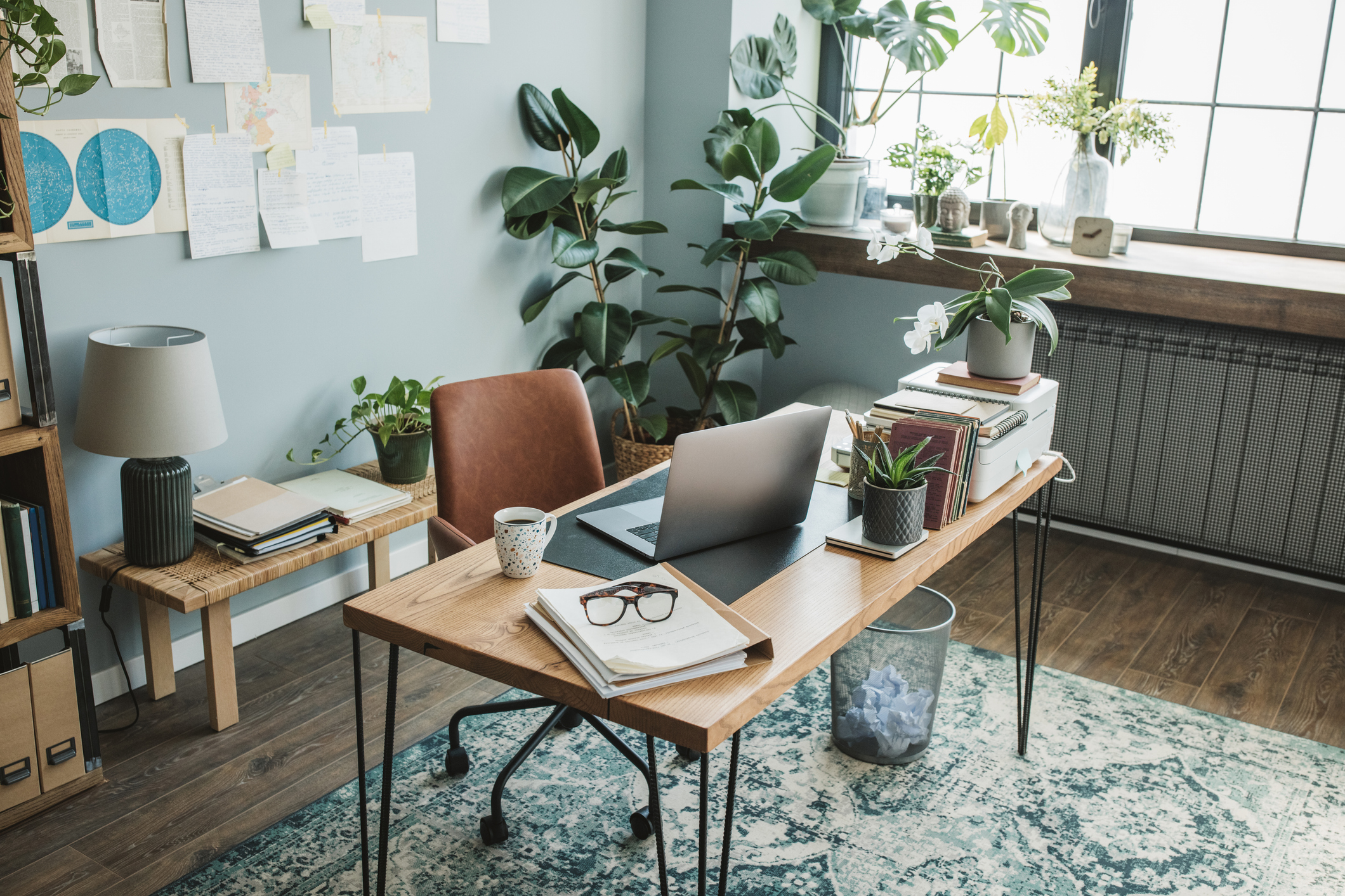 The modern pine-topped desk of an understated home office uses book pages and maps pinned to the wall as the backdrop for video meetings.