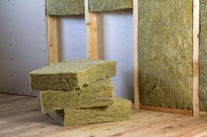 A stack of three rockwool insulation sheets sits next to a wall frame in the process of being insulated.