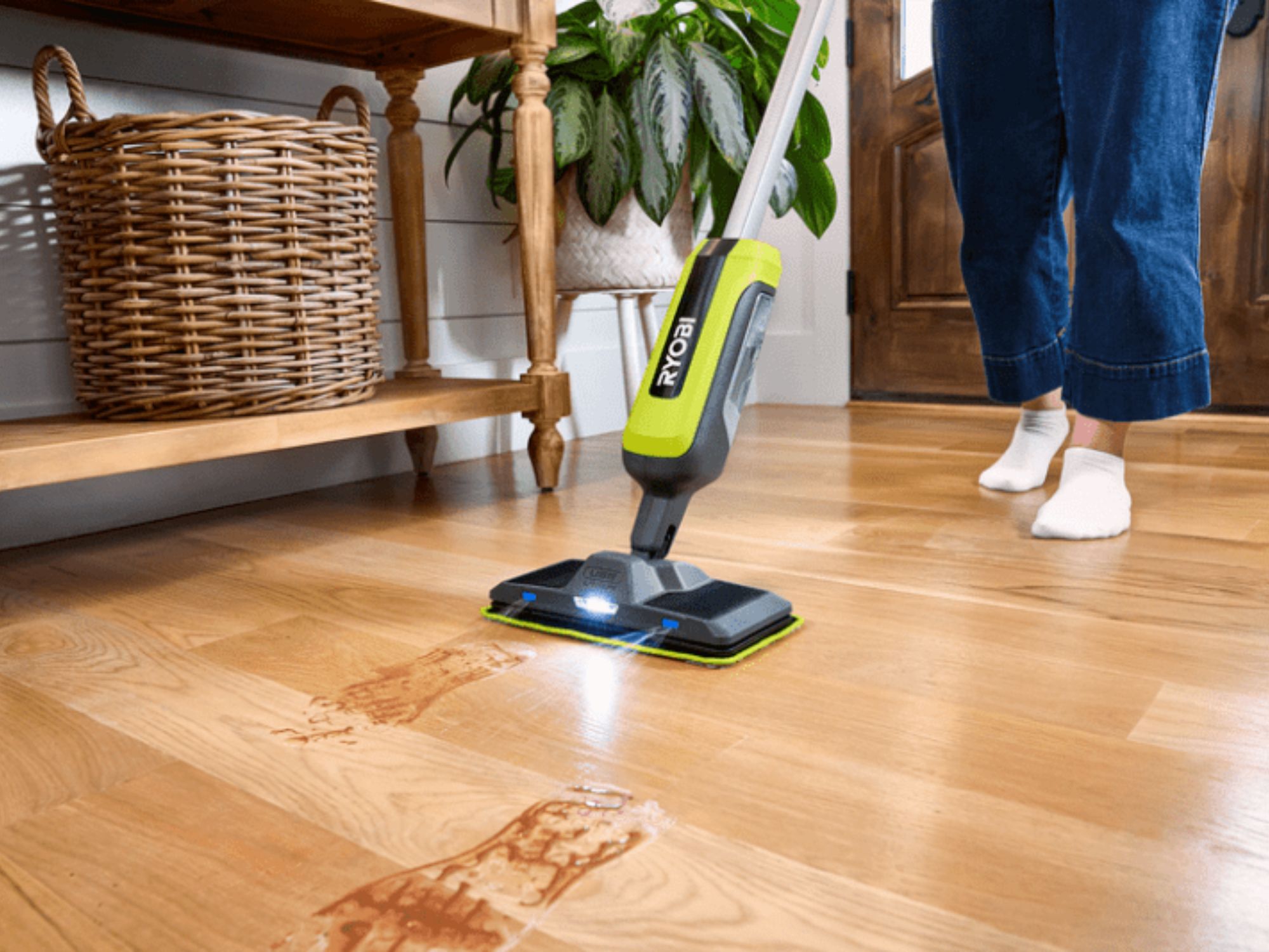 Person wearing jeans and white socks mopping a wood floor with a Ryobi spray mop