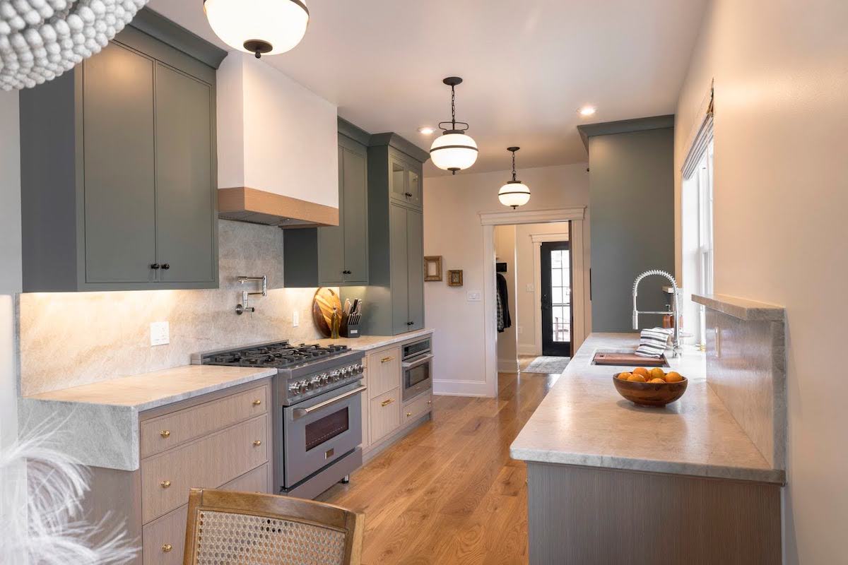 A galley kitchen with hardwood floor and grey cabinets features a slim grey oven that fits the small space.