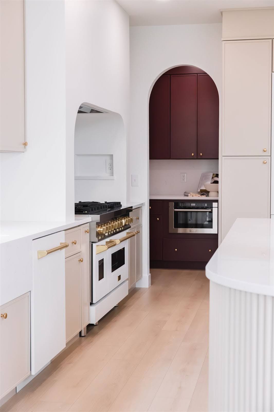 A galley kitchen with mostly white counters and cabinets features a pop of mahogany-colored cabinets. 