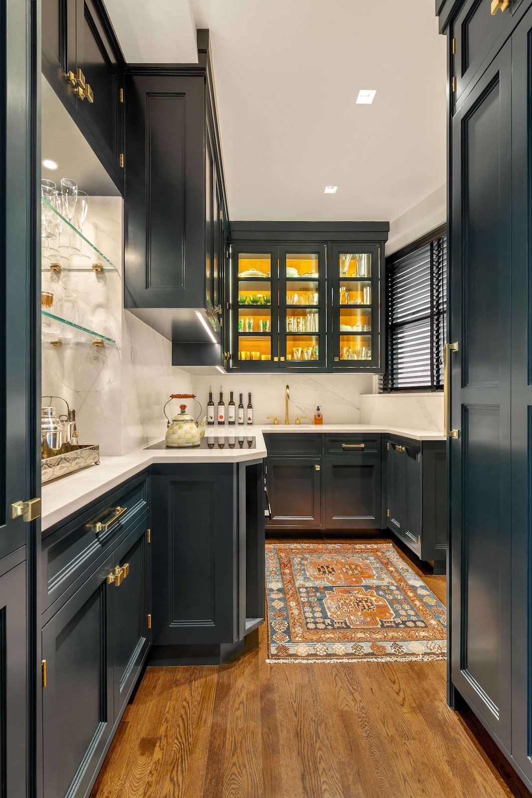 A cozy galley kitchen with a rug on the hardwood floor features dark green cabinets.