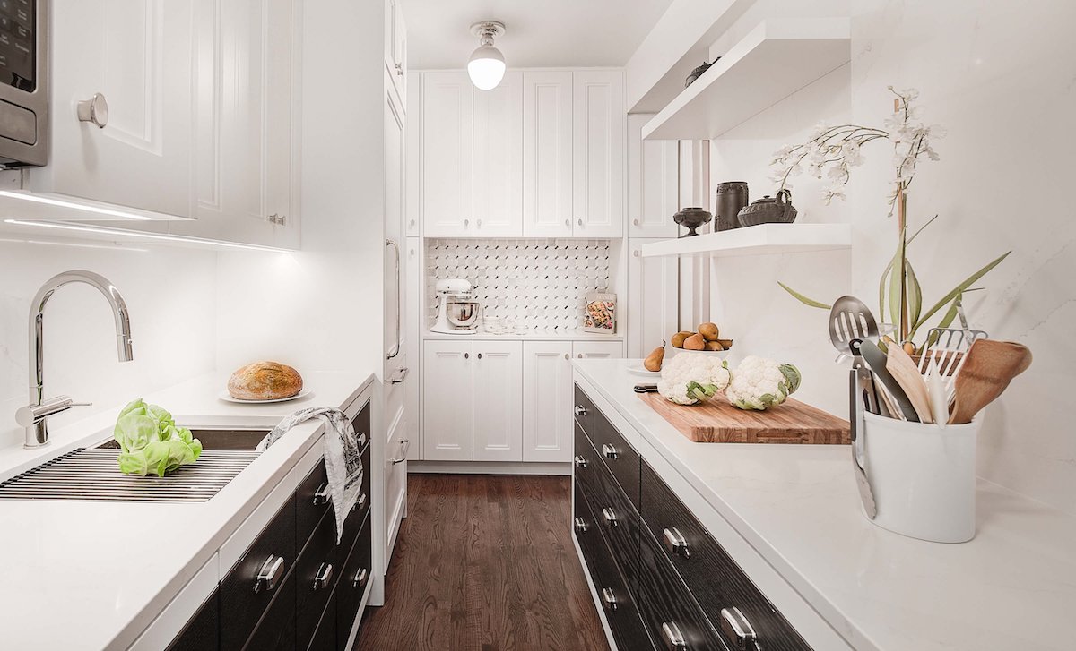 A galley kitchen features contrasting white countertops and upper cabinets and black lower cabinets.