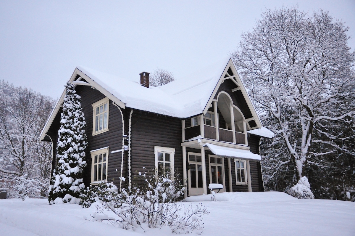 A traditional-style home with brown siding and brick chimney on a snowy day.