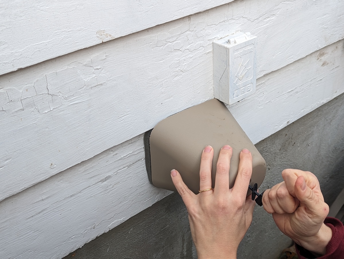 A homeowner installing a faucet protector over an exterior spigot for winterization. 