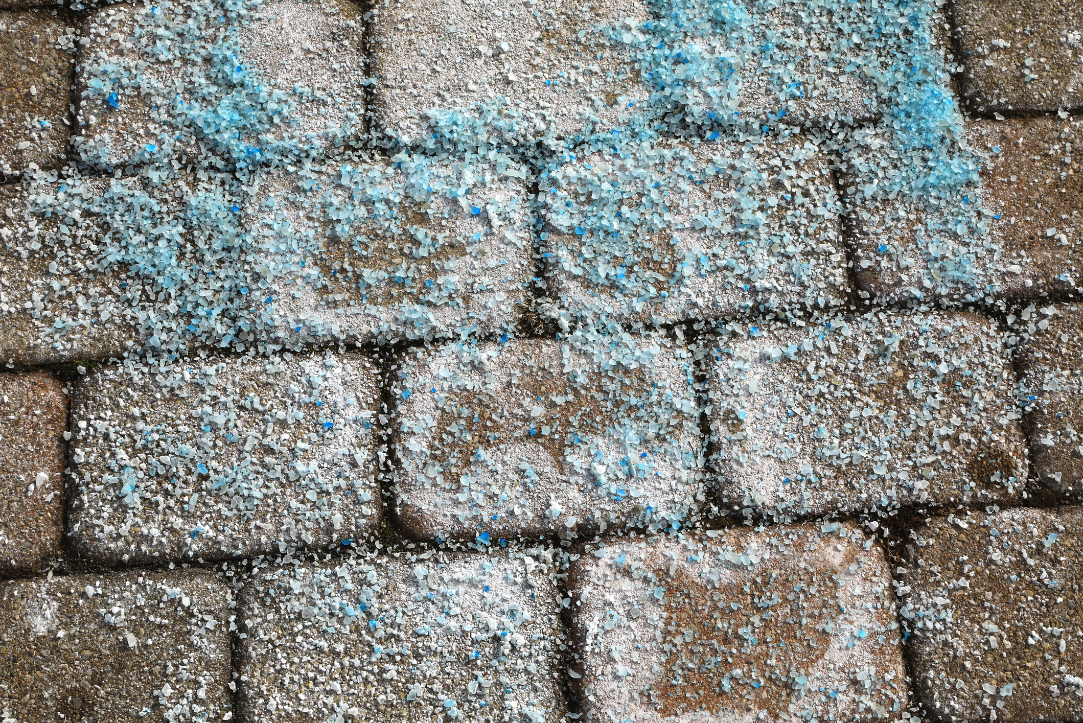 Blue dyed ice melt crystals on a paved sidewalk for snow removal.