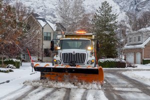 Snowplow driving through residential neighborhood with snow on the ground.