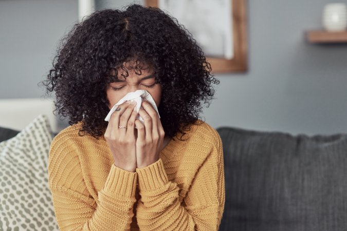 Young woman blowing her nose with a tissue at home on her couch.