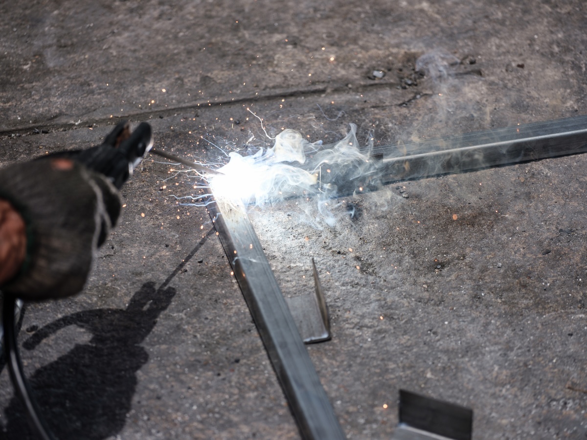 A person using a stick welder to weld metal parts together in a home workshop.