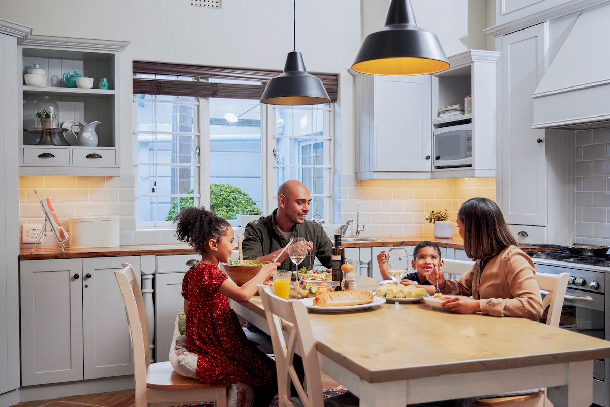 A family eating together at the kitchen table lit by pendant lights overhead.