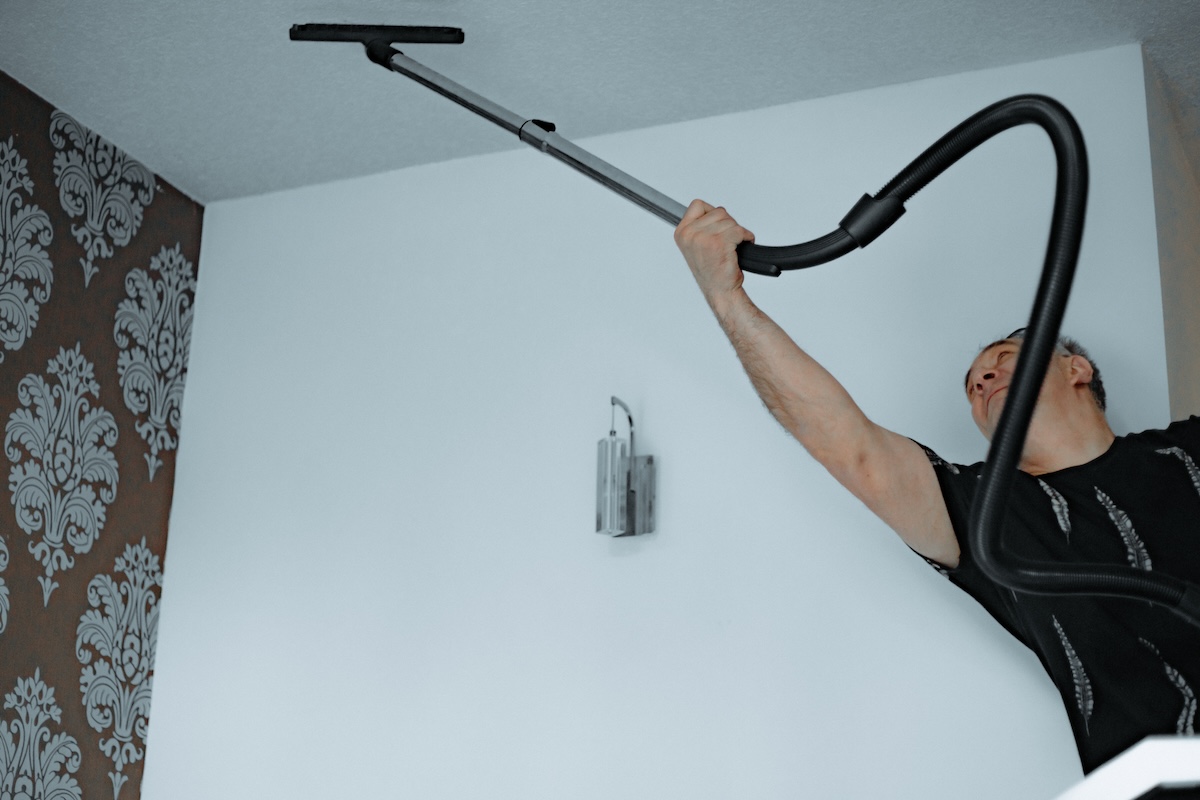 A homeowner reaches a vacuum across the ceiling to clean up bugs inside a house.