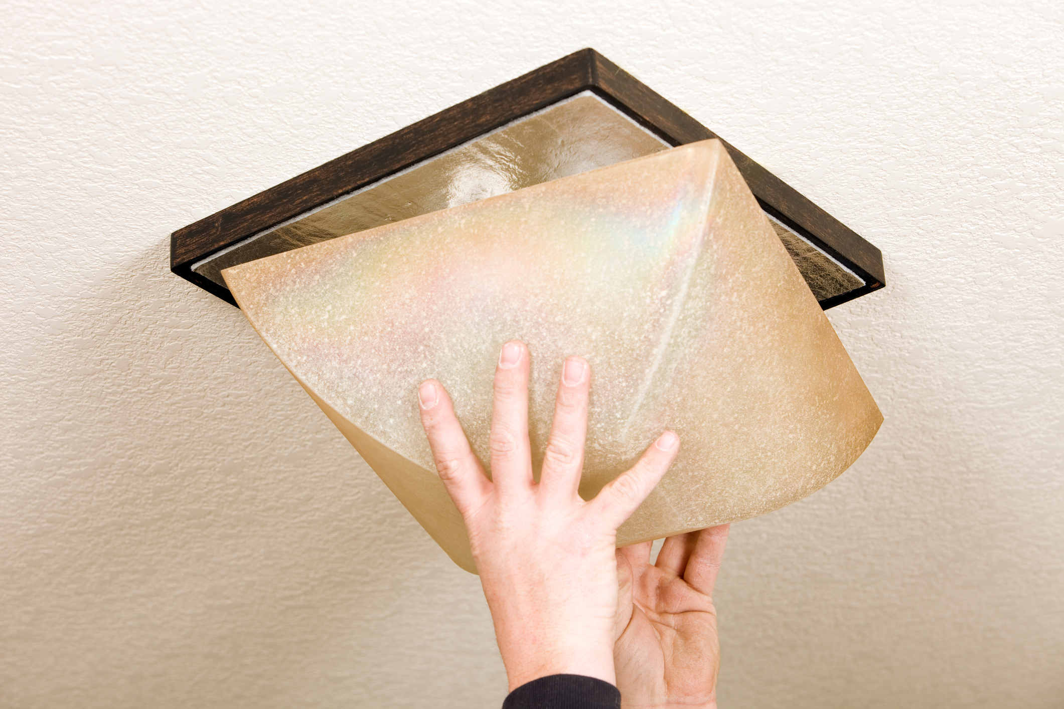 Hands of a person installing a flush-mount ceiling light fixture.