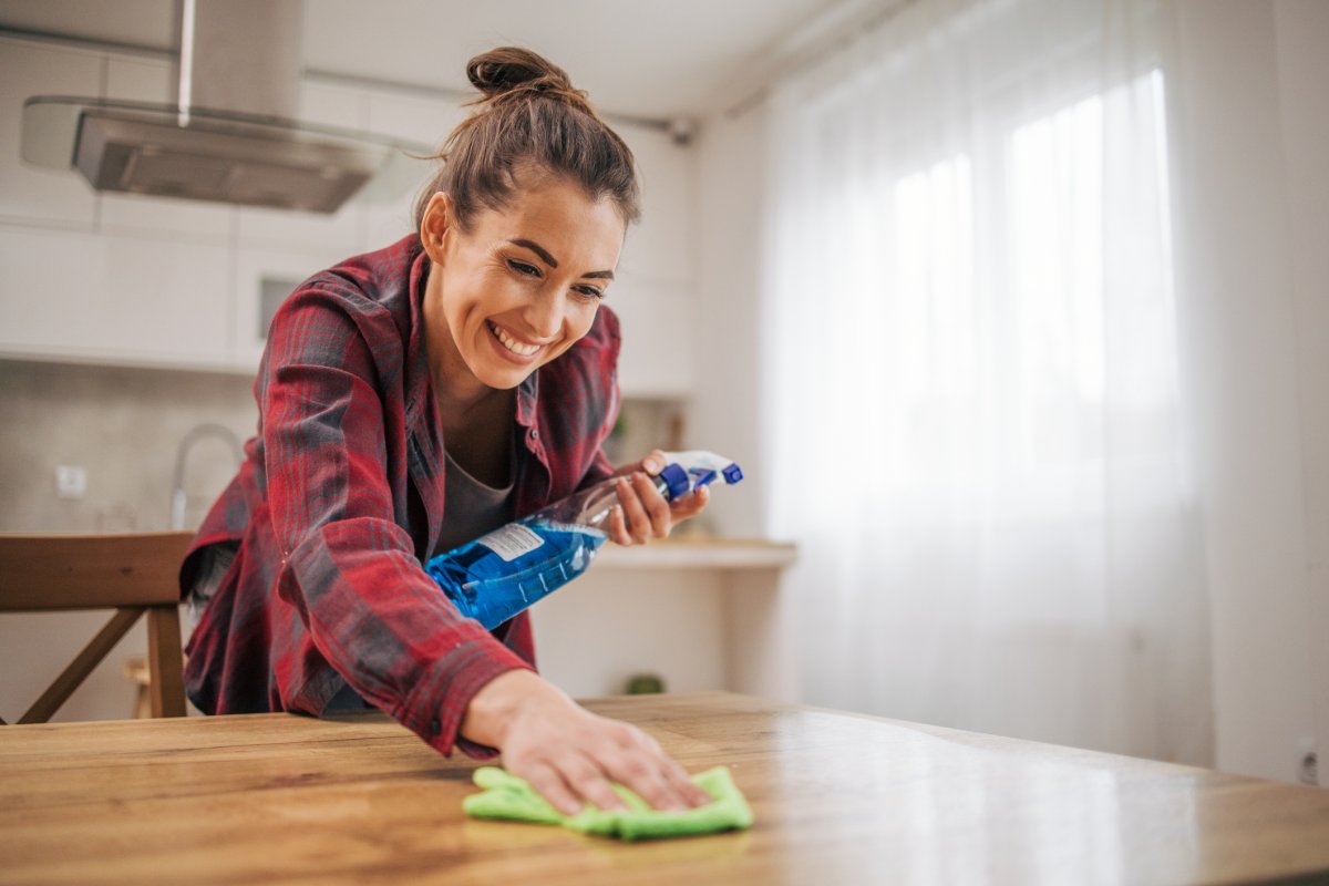 A happy woman keeps her home clean by wiping off the kitchen table. with a rag and a sprayer.