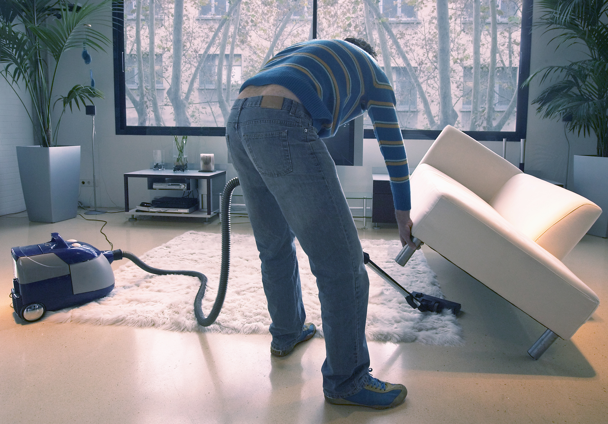 Man vacuuming under a white couch.