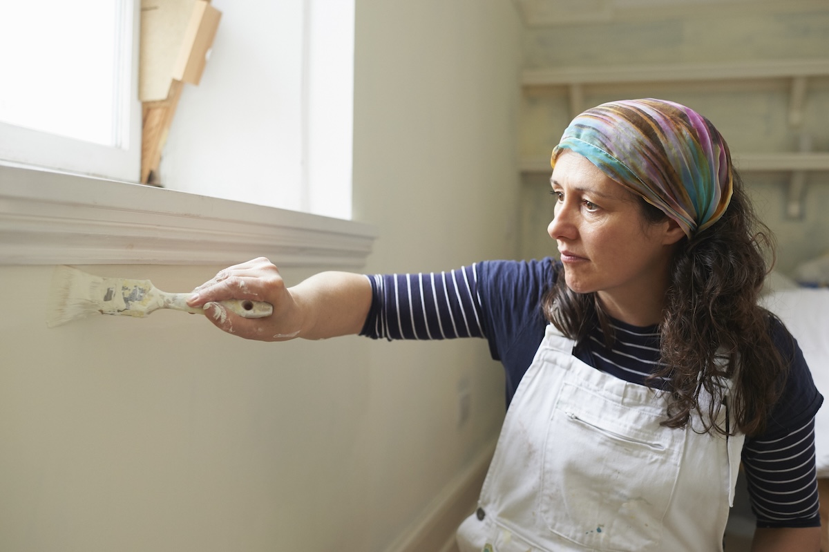 A person touching up paint on walls inside a home.