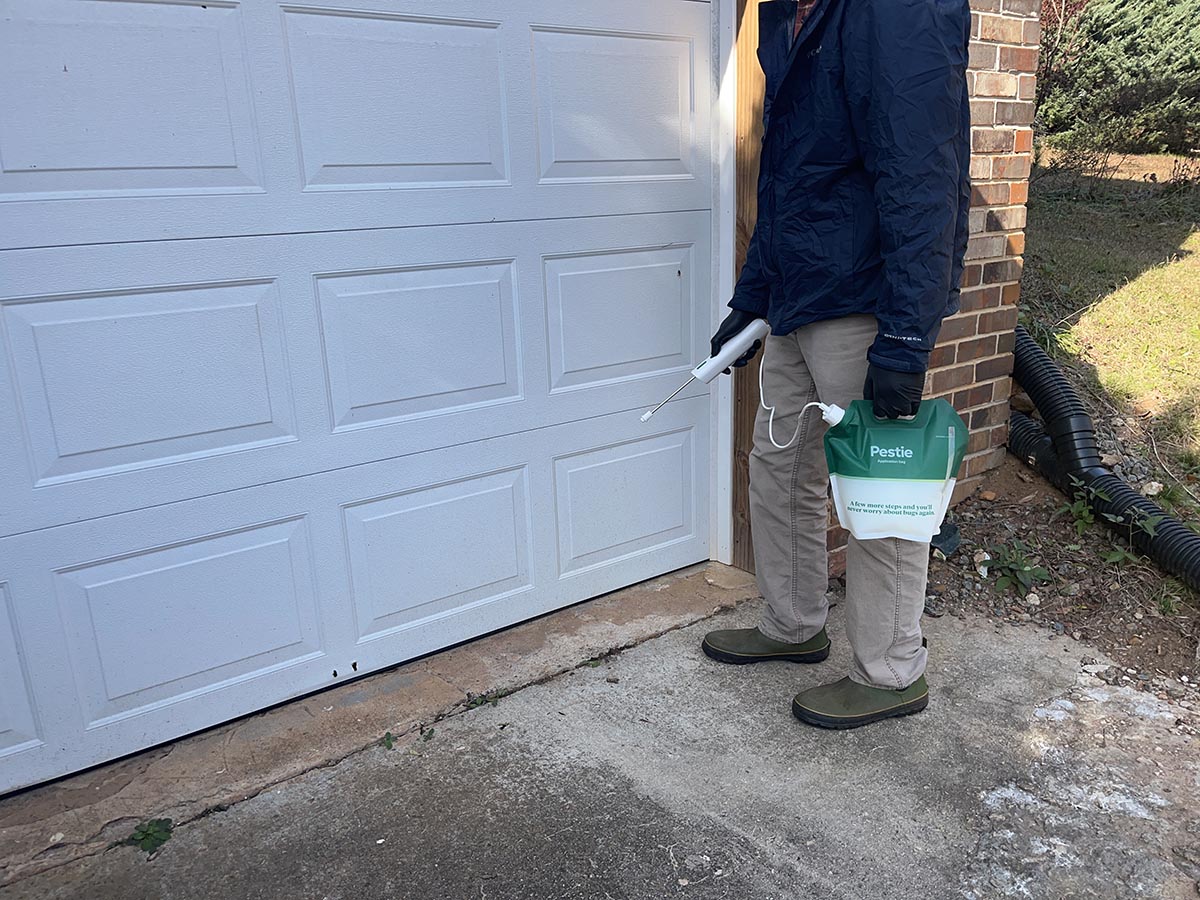 Person spraying Pestie insecticide along the perimeter of garage door