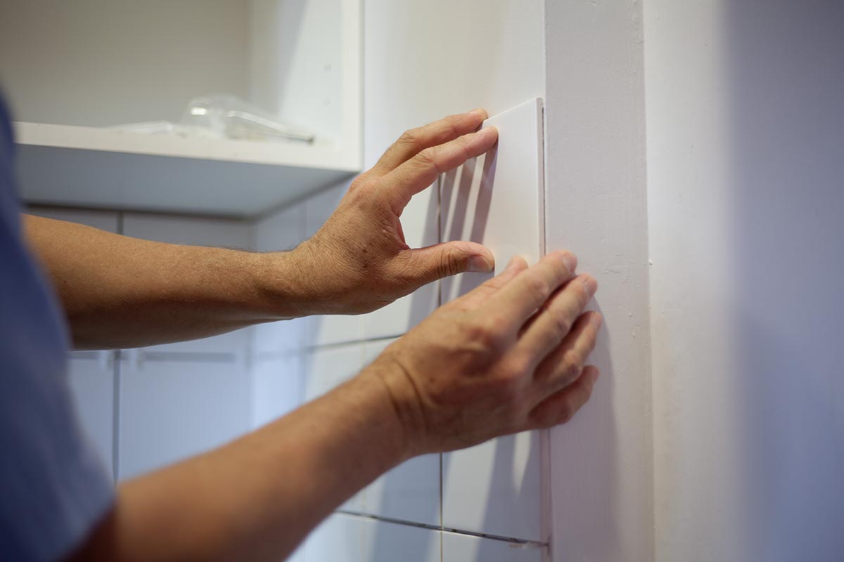 A person repairing a broken wall tile using just glue.