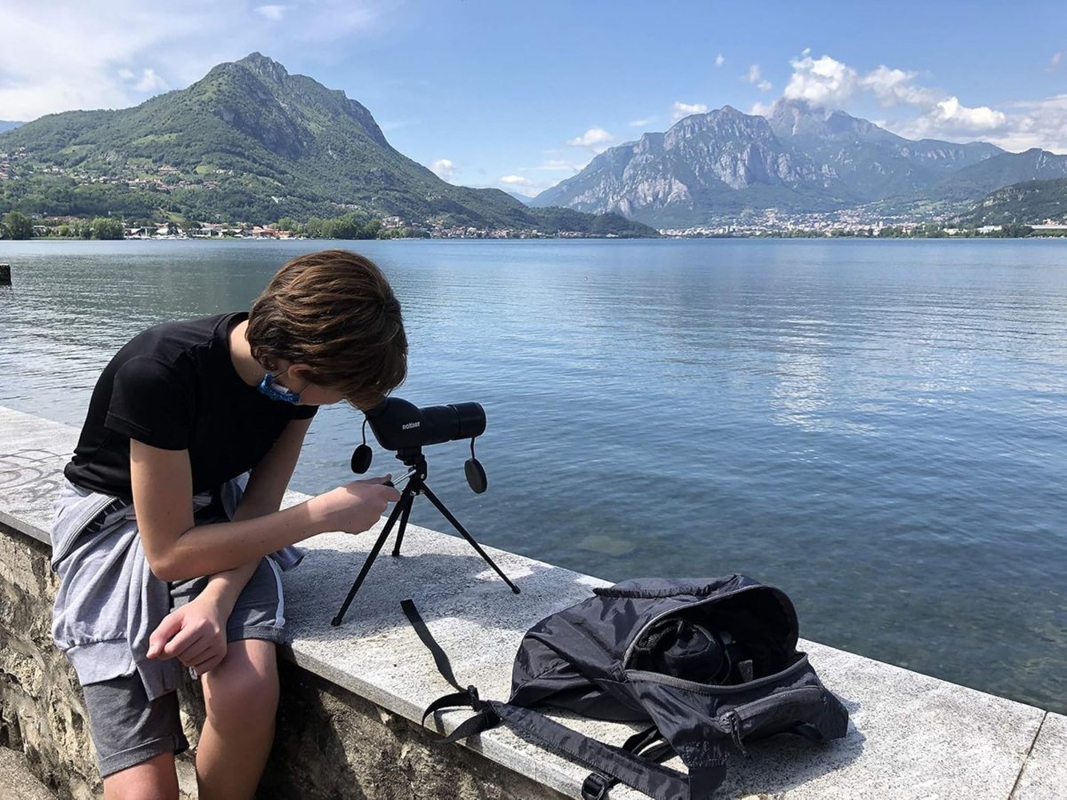 a boy at a lake looking from a compact spotting scope