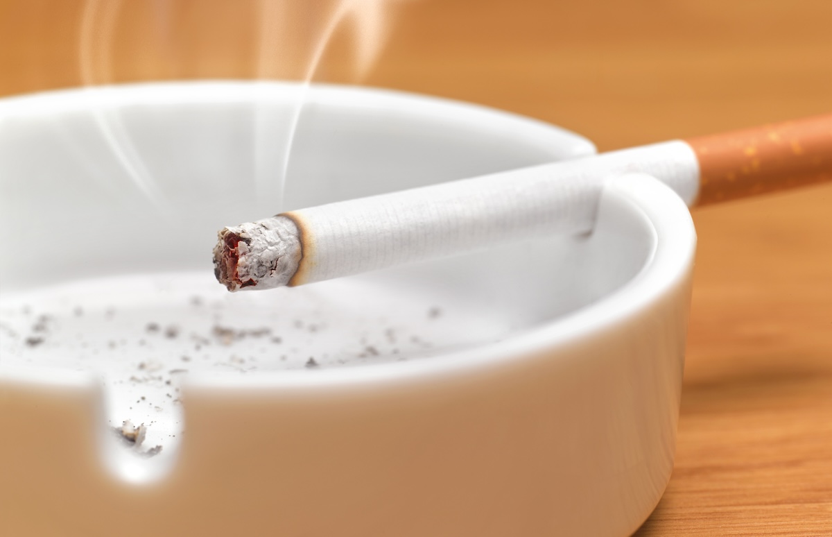 A cigarette resting in a white ashtray.