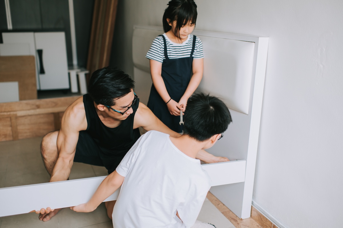 A father and his young son and daughter fix a modern bed frame.