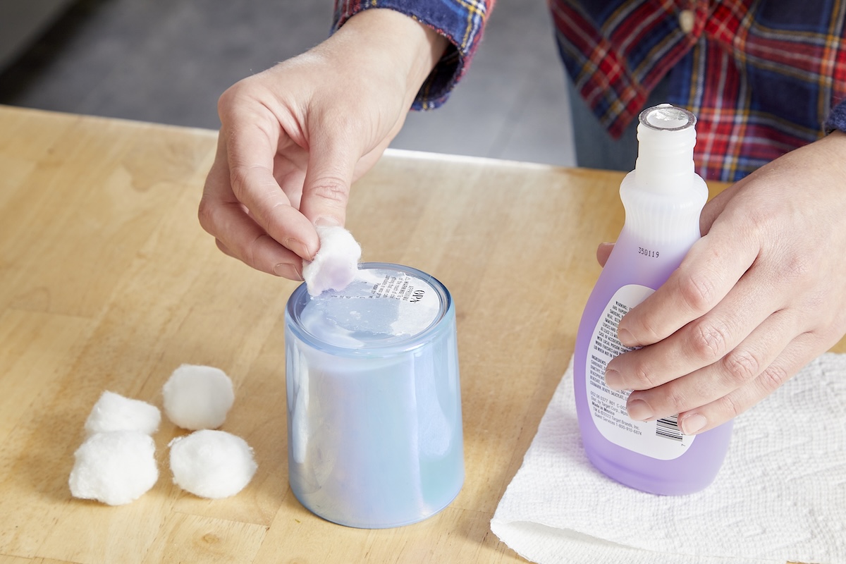 A person removing glue from bottom of candle jar using nail polish remover.