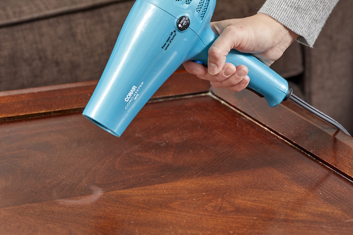 A person using a hair dryer to remove water stains from wood.