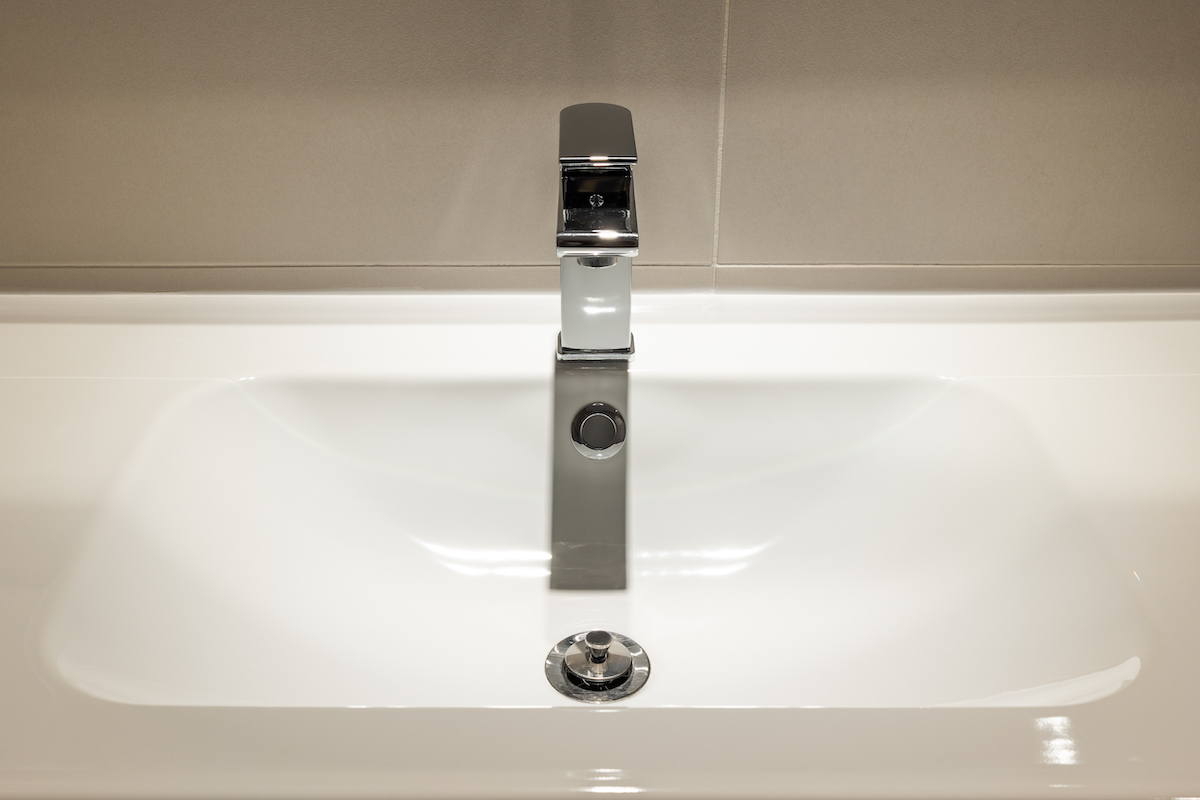 Close-up of new stainless faucet on clean wash sink in modern bathroom.