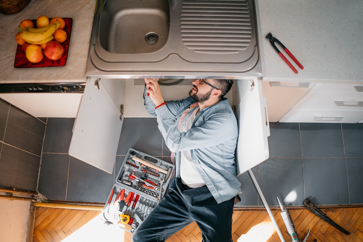 A man with a blue shirt lays beneath a kitchen sink to repair the drain.