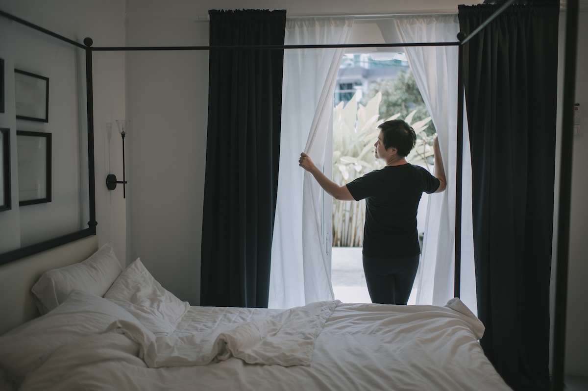 A woman opens her soundproof bedroom curtains.