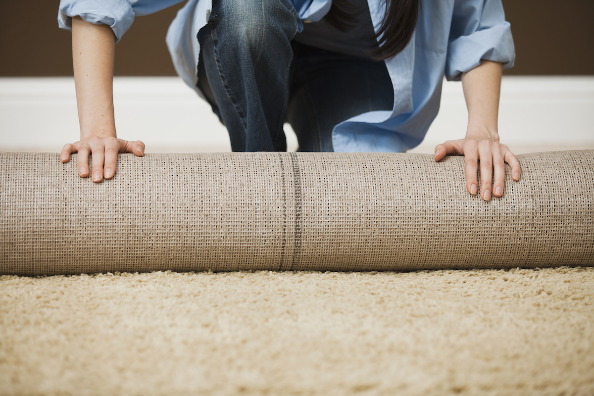 Direct image of woman (head not shown) unrolling a large carpet.