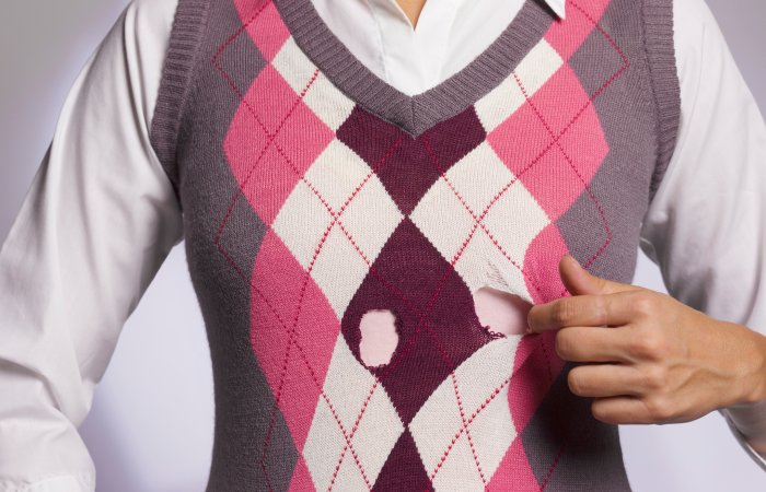 Faceless woman pointing to holes in her pink and gray sweater.