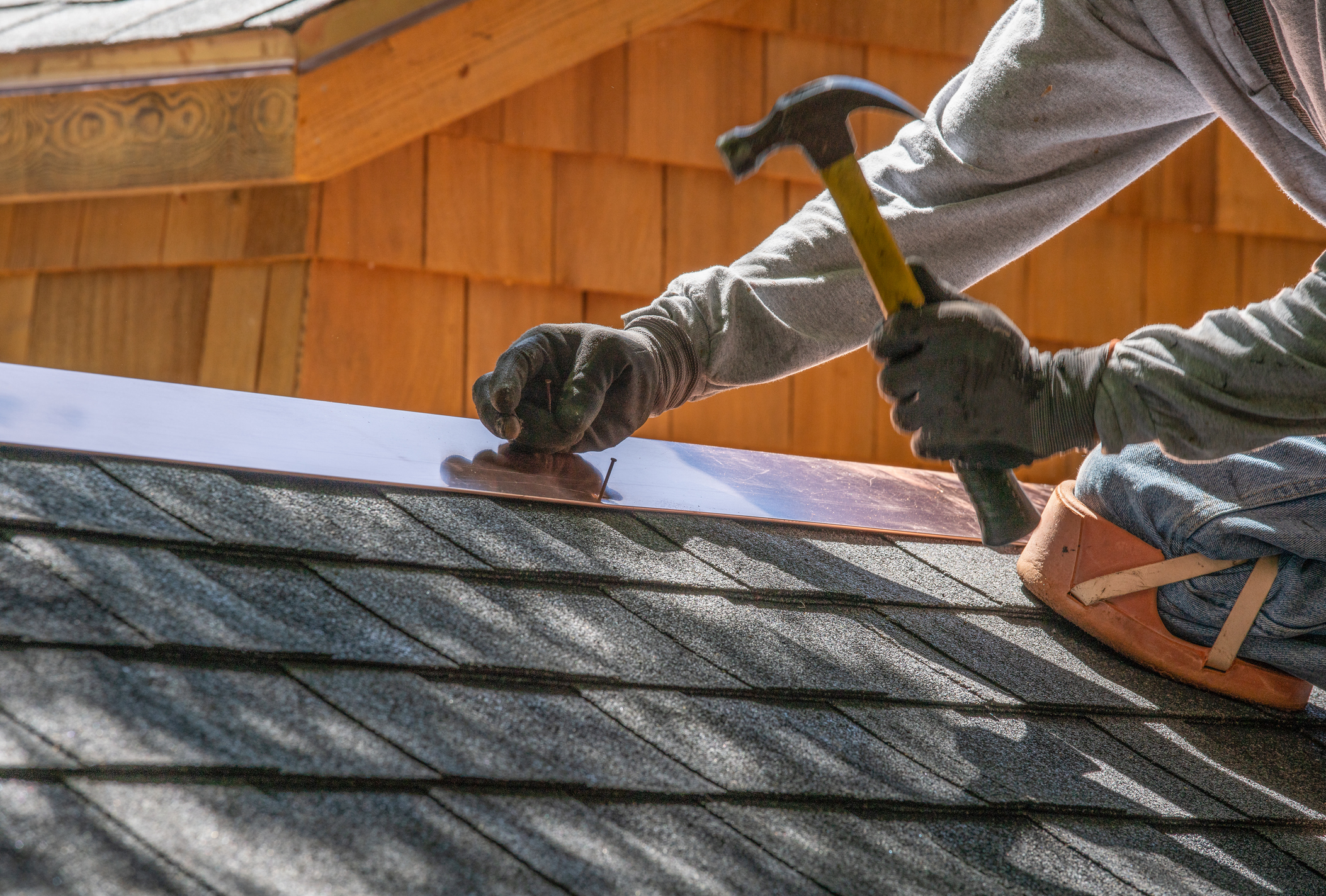 Faceless person installing a new roof shingles with nail gun and hammer.