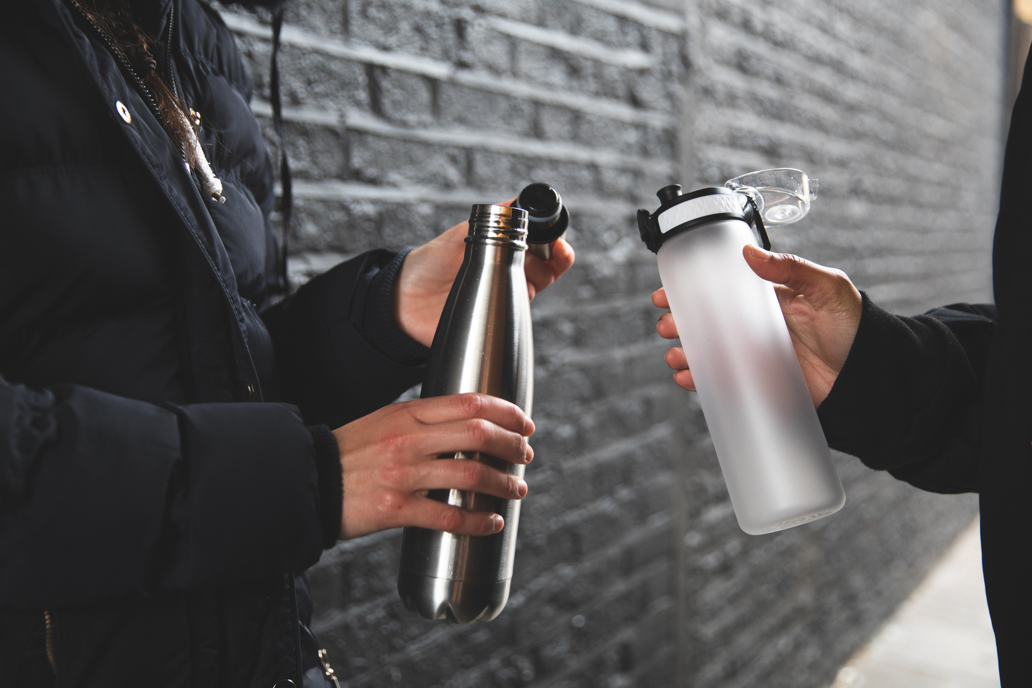 Women holding reusable water bottles with a brick wall background.