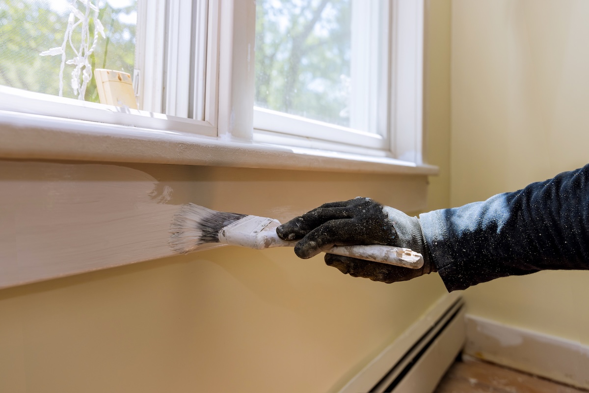 A person painting over window trim repaired with all-purpose putty like Bondo.