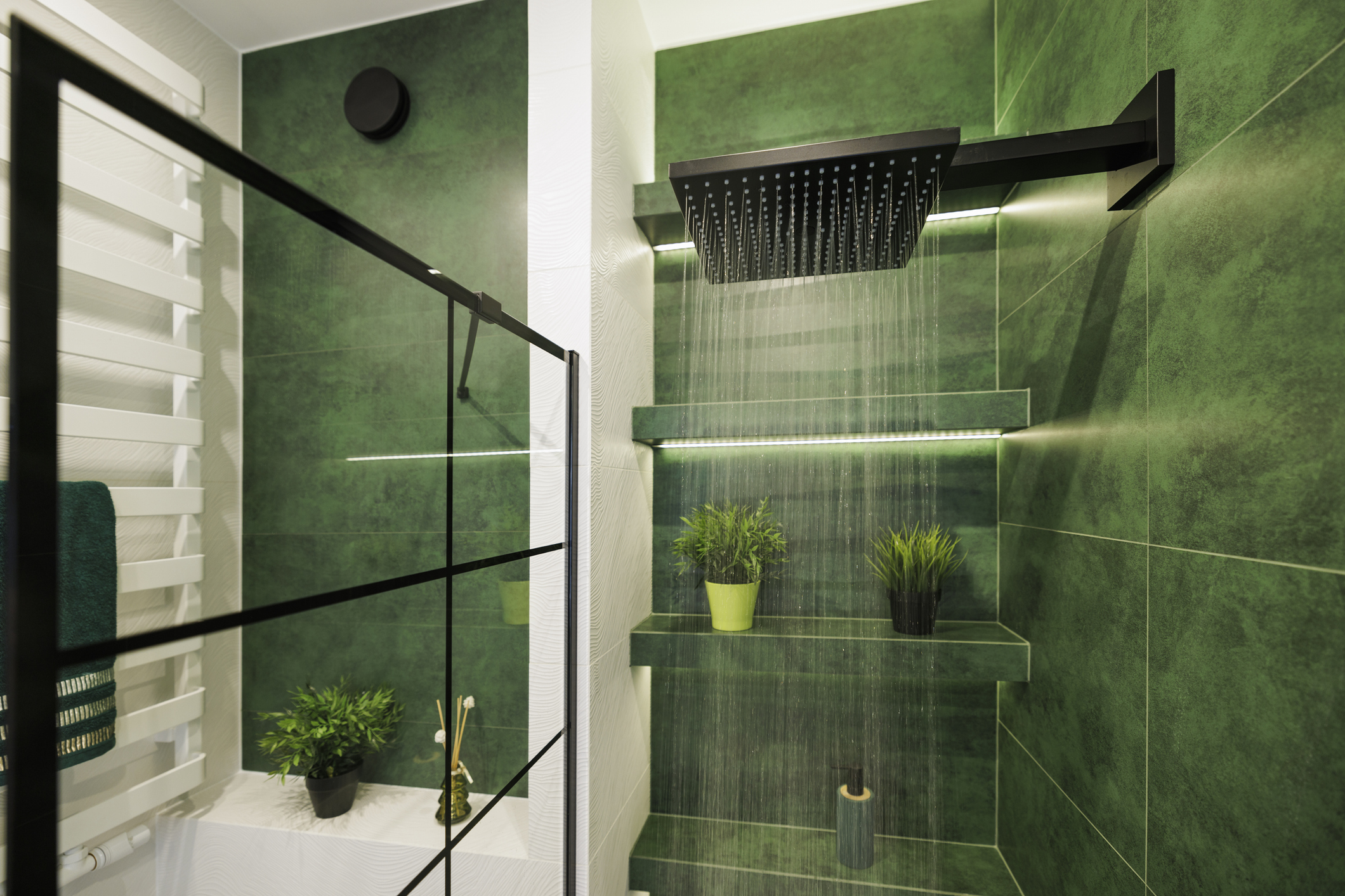 Modern luxury bathroom with green and white tiles. Water running from a black rain shower head.